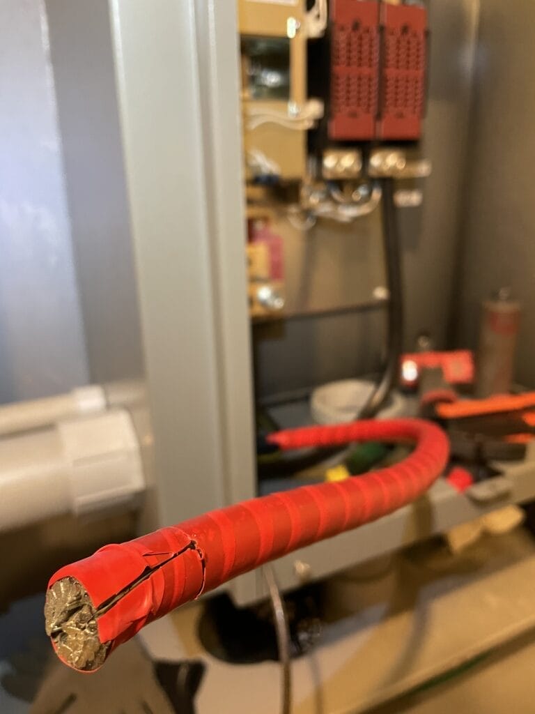 Close-up of a cut end of a red insulated wire in front of electrical equipment in a panel near Bayonet Point FL